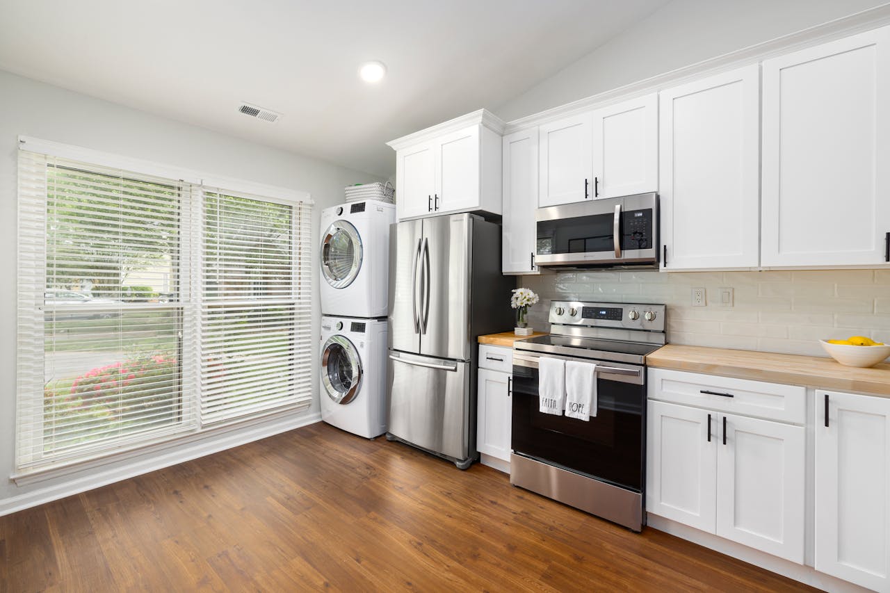 about-01 A modern kitchen featuring stainless steel appliances, white cabinets, and a wooden floor with ample natural light.
